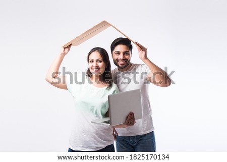 Indian young family couple choosing new home online, search real estate to buy or rent, house for sale on screen of computer, standing against white background