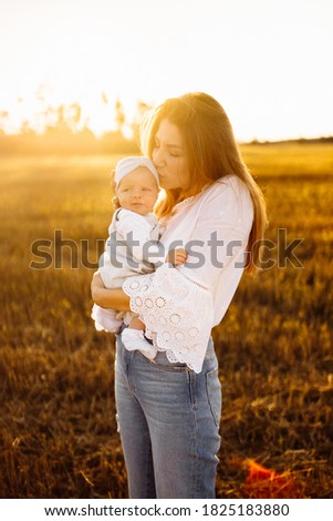 Adorable mother with beautiful little daughter at the field, pretty woman hold cute newborn baby in arms, caring mom gently kiss tiny baby girl, maternity concept. High quality photo