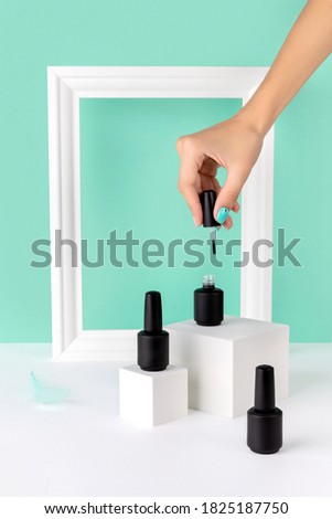 Bottle of nail varnish on podium with womans hand on turquoise background. Beauty salon product mock up template in minimal slyle. Royalty-Free Stock Photo #1825187750