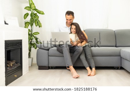 Happy family with kid girl having fun using laptop together sitting on sofa, parents and child daughter laughing relaxing at home with computer watching funny internet video, making online call