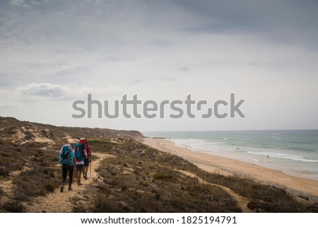 Three hikers walk the trail along the dunes, standing aside a beach landscape on a grey day