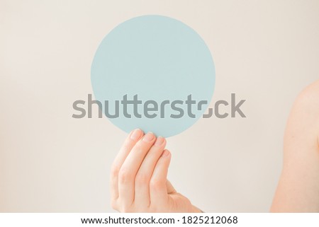 Round blue card with copy space in the hand of a young woman. Pastel blue color postcard layout. Informational round plate about a discount, opening, new product, advantageous offer.
