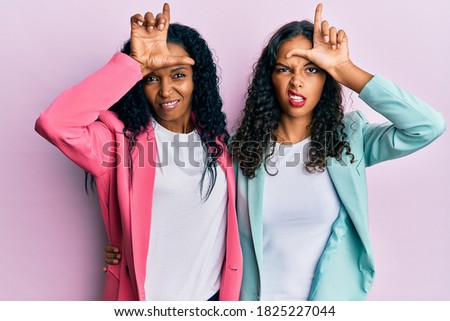 African american mother and daughter wearing business style making fun of people with fingers on forehead doing loser gesture mocking and insulting. 