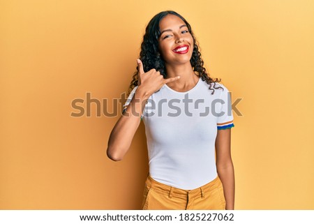 Young african american girl wearing casual clothes smiling doing phone gesture with hand and fingers like talking on the telephone. communicating concepts. 