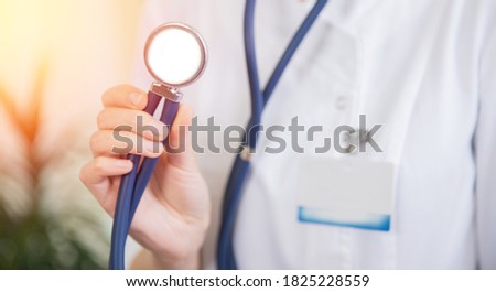 Doctor woman holding aStethoscope or phonendoscope on background of white medical gown, preparing to receive patient light sun.