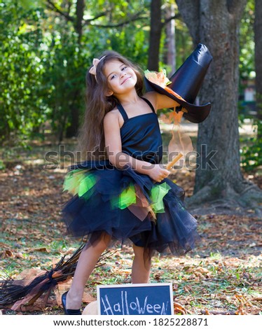 a little girl with black hair in a witch costume with a broom in her hands. Halloween