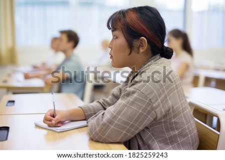 Portrait of focused japanese teenage schoolgirl writing lectures in workbooks in classroom during lesson