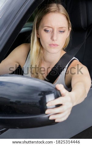 woman adjusting side mirror of blue car in nature