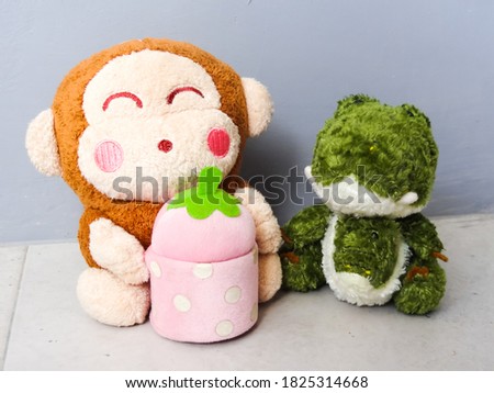 a small green crocodile doll and her friend on a gray background