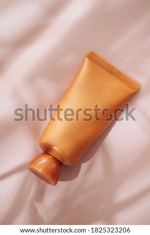 Orange cosmetic beauty tube from above on pastel background. Brand aad mockup. Lights and shadows from palm leaves. Copy space, minimalism