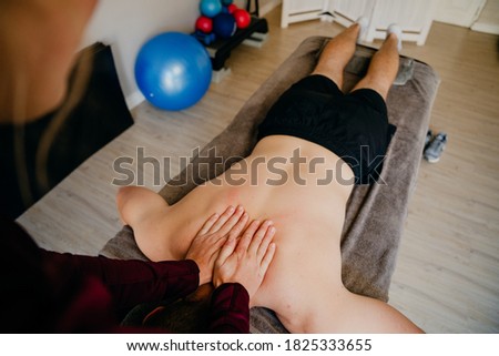 physiotherapist lightly pressing down on neck of patient lying on massage bed in sports studio.