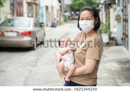 Asian mother wearing surgical face mask holding her baby, COVID-19 concept