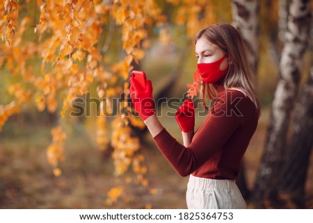 Active young woman in red gloves and face mask at autumn park with mobile phone