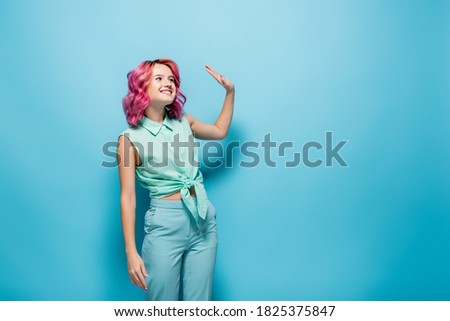 young woman with pink hair waving hand on blue background