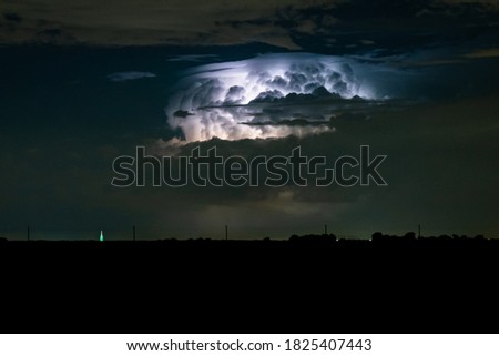 Distant supercell thunderstorm is lit by lightning at night. At the top of the storm cloud, a double cap is visible, known in meteorology as pileus.