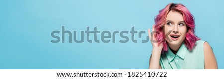 curious young woman with pink hair listening isolated on blue, panoramic shot