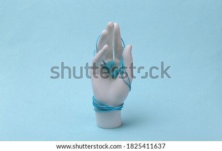 White mannequin hand wrapped in earphones on blue background