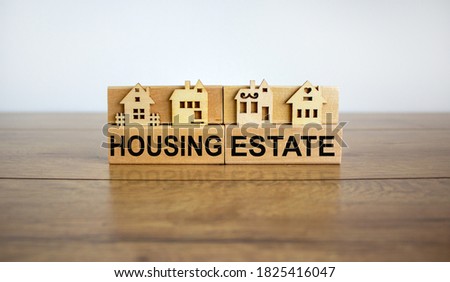 Wooden blocks form the words 'housing estate', miniature house, wooden table. Beautiful white background, copy space. Business concept.