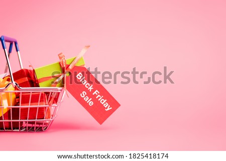 shopping basket with gifts and red tag with lettering on pink, black friday concept