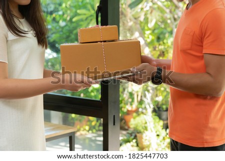 Delivery service worker in uniform delivering parcel to recipient. Woman signing e-document on tablet.