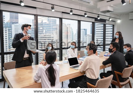 Caucasian businessman presentation of business plan on laptop at conference table, Group of business people wearing face mask meeting in modern office while pandemic of Coronavirus, Covid 19 Royalty-Free Stock Photo #1825464635