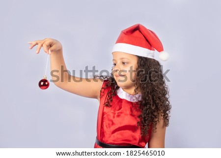 Little Brazilian girl dressed as Mama Claus holding a Christmas ball on white background, selective focus.