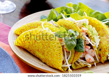 Vietnamese Banh Xeo crepes filled with pork or chicken may also, shrimp, onions and bean sprouts, and hot sauce placed near the plate on the table Royalty-Free Stock Photo #1825503359
