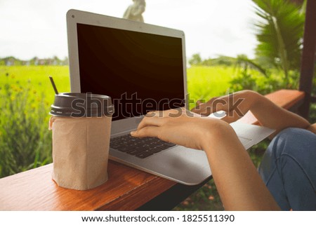 Close-up of hands using laptop on the wooden table. Hands typing on the keyboard. Blurred of green leaf background. Working out door concept.