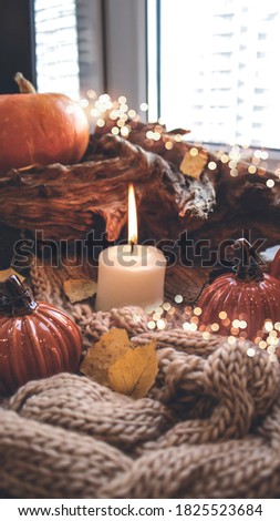Candle on an autumn background with pumpkins, dry leaves, bokeh lights. Knitted warm blanket.