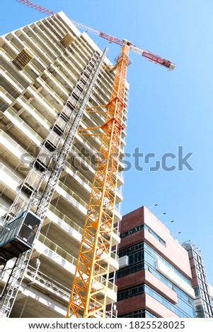 Low angle view of yellow construction plane building a tall edifice. 
