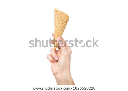 Ice cream cone in hand. Concept of eating ice cream. A man holds a waffle without ice cream in his hand on a different light background.