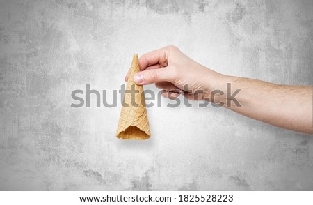 Ice cream cone in hand stone background. Concept of eating ice cream. A man holds a waffle without ice cream in his hand on a different light background.