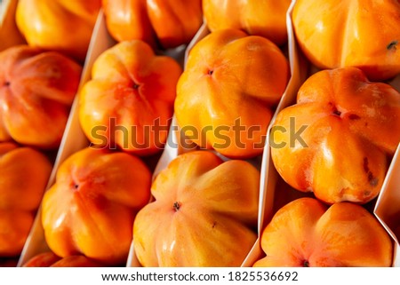 A lot of bright ripe persimmon of the chamomile variety in a box. Seasonal autumn fruit. Close-up.