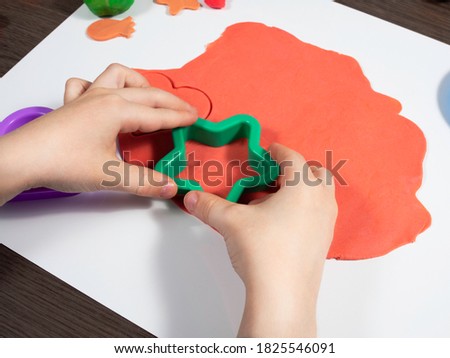 Child is making a star with red play dough using a shape. Kids hands close up.  Royalty-Free Stock Photo #1825546091