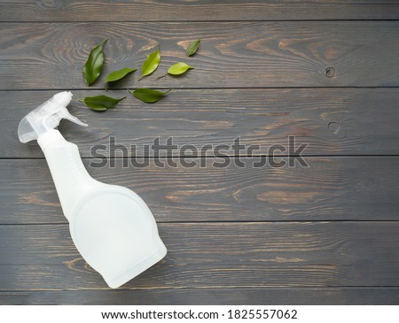 Plastic bottle with liquid for cleaning glass, plumbing, tiles or floor and green herbal leaves on a gray wooden background with space for text. Natural organic cleaning product. Eco-concept. Poster. Royalty-Free Stock Photo #1825557062