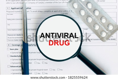 Magnifying glass with text Antiviral Drug inside lies on medical documents with pills and a blue metal pen. Can be use as a concept photo