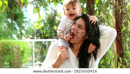 Cute mother and baby son caring and loving relationship. Casual infant sitting on mom shoulders