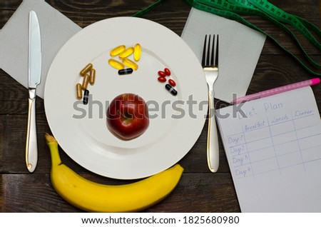 Drawing up a diet. Pills in a plate with an apple on a wooden table. Cutlery and diet drawing up on a wooden table. Diet concept.