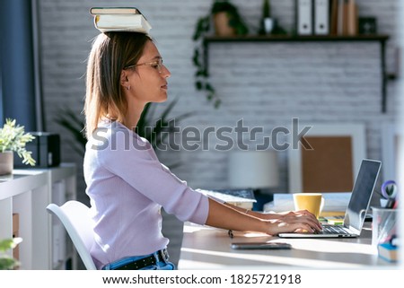 Shot of young attractive woman at the desk with books on her head while working with computer at home. Royalty-Free Stock Photo #1825721918