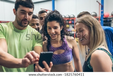 Group of athletes laughing looking at the mobile of a gym mate