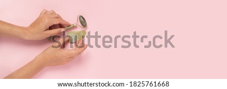 Guasha green natural gemstone face roller on pink background. Anti aging self care tool. 
