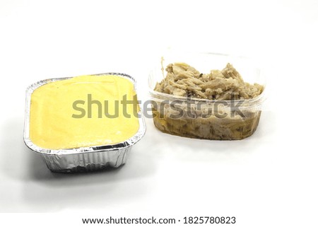 A closeup of polenta in a tub and cooked cod in a plastic container on a white background