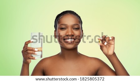 beauty and people concept - portrait of happy smiling young african american woman with cod liver oil and glass of water over lime green natural background