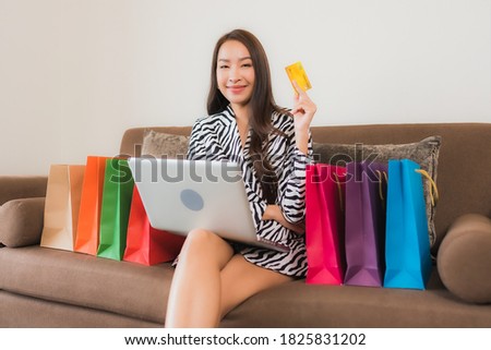 Portrait beautiful young asian woman use computer laptop , smart mobile phone or cash money for online shopping on sofa in living room interior