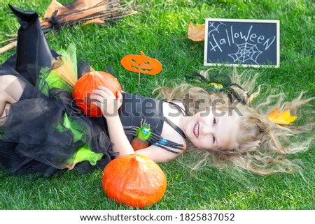girl in a witch costume for the Halloween holiday. Placard with the inscription: Halloween. Happy girl lies on the grass
