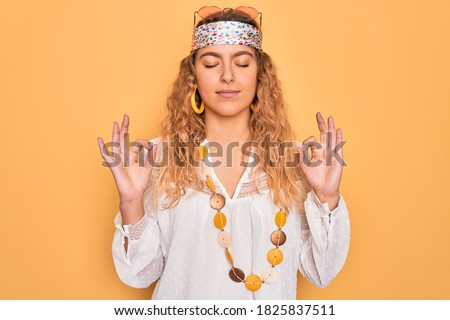Young beautiful blonde hippie woman with blue eyes wearing sunglasses and accessories relaxed and smiling with eyes closed doing meditation gesture with fingers. Yoga concept.