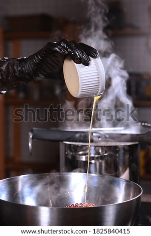 The chef adds olive oil to a metal bowl. Steam from the pan. Unrecognizable vertical photo.Hand in a black protective glove. Close up.