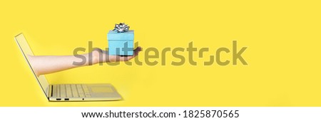 Giving a gift from the screen of the computer online yellow background and blue present with the silver bow on the top of it