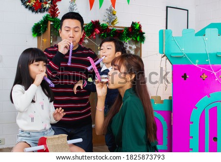 Asian family father, mother, daughter, son blowing party horn blower at party.