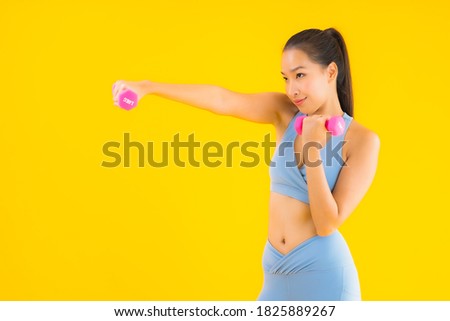 Portrait beautiful young asian woman with dumbbell and sportwear ready for exercise on yellow isolated background